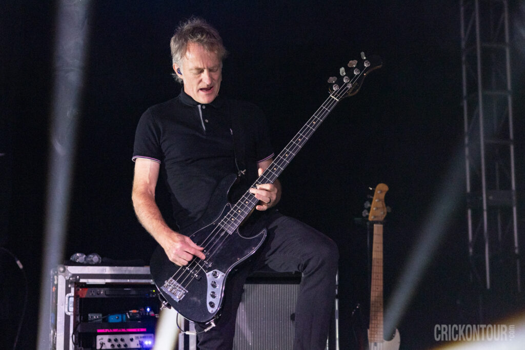 Bass guitarist Duncan Coutts of Our Lady Peace plays a black bass on a dark stage, wearing a black polo shirt, eyes closed in concentration.